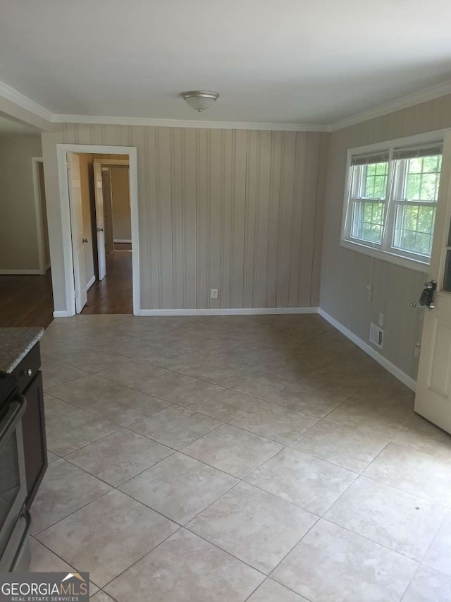 empty room with baseboards, light tile patterned floors, visible vents, and crown molding