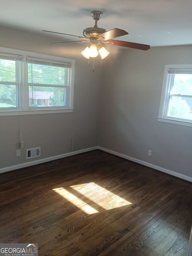 unfurnished room with plenty of natural light, baseboards, visible vents, and dark wood finished floors