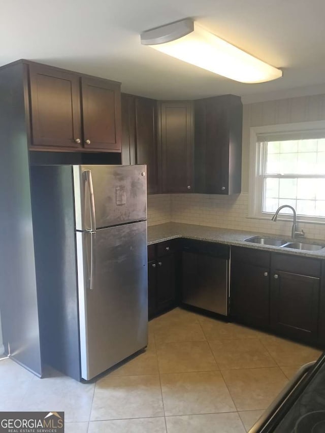kitchen with light tile patterned floors, stainless steel appliances, decorative backsplash, a sink, and dark brown cabinetry