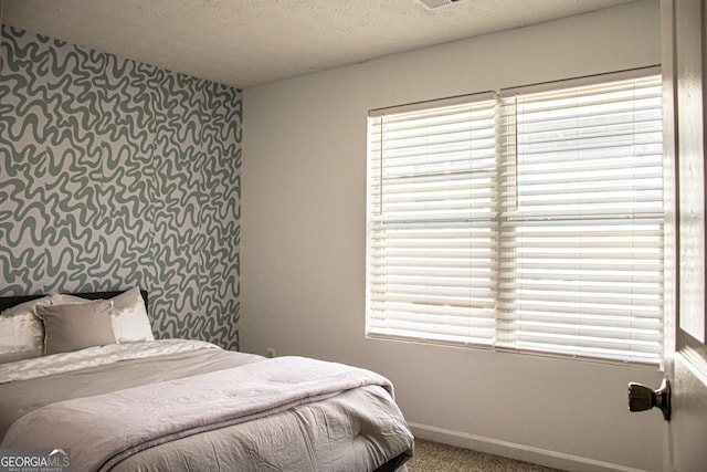 bedroom with baseboards, a textured ceiling, an accent wall, and carpet