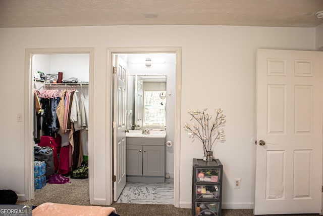 bedroom with a closet, light carpet, a walk in closet, a textured ceiling, and ensuite bath