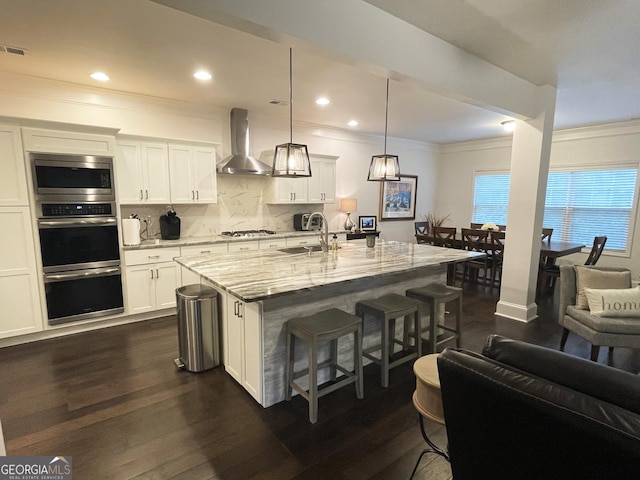 kitchen with wall chimney exhaust hood, a sink, a kitchen bar, light stone countertops, and stainless steel appliances