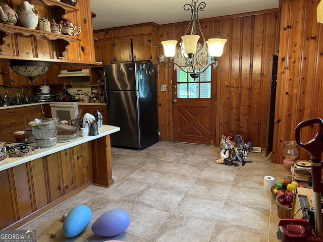 kitchen with light countertops, white range with gas cooktop, under cabinet range hood, brown cabinetry, and freestanding refrigerator