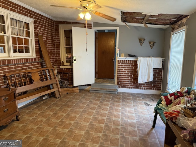 interior space with ceiling fan, a healthy amount of sunlight, ornamental molding, and brick wall