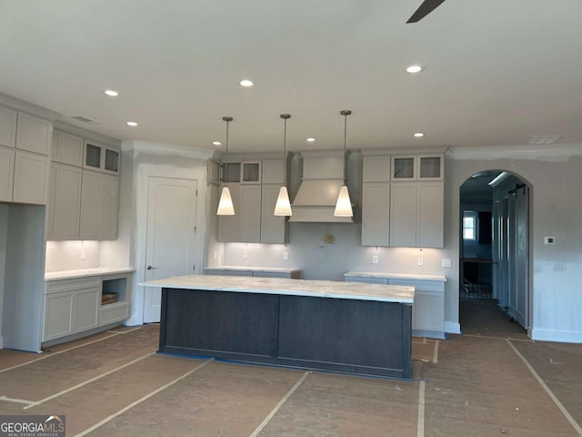 kitchen featuring a kitchen island, glass insert cabinets, custom exhaust hood, arched walkways, and recessed lighting