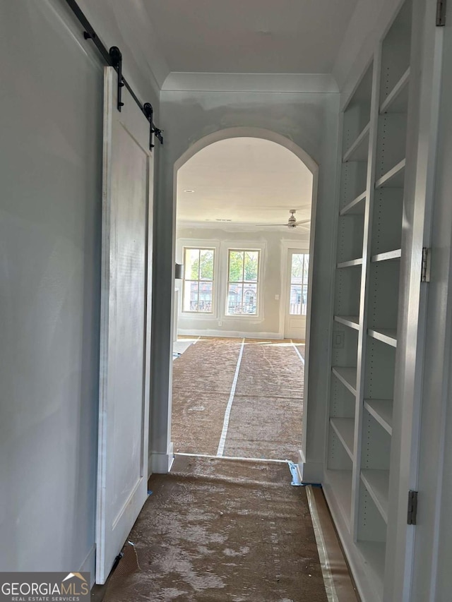corridor with a barn door, arched walkways, and ornamental molding