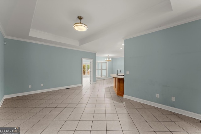 spare room with baseboards, an inviting chandelier, a sink, ornamental molding, and a tray ceiling