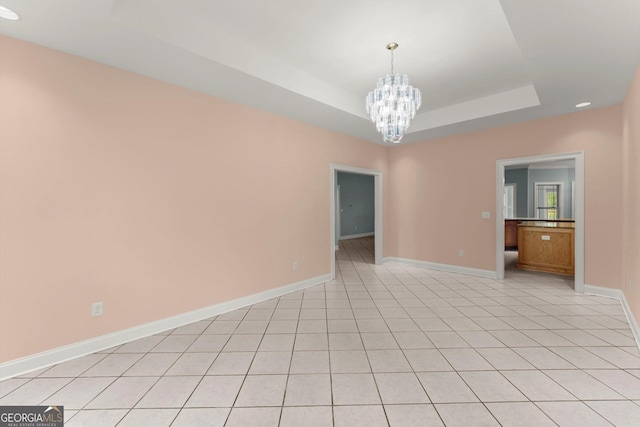 unfurnished room featuring a tray ceiling, baseboards, recessed lighting, and an inviting chandelier