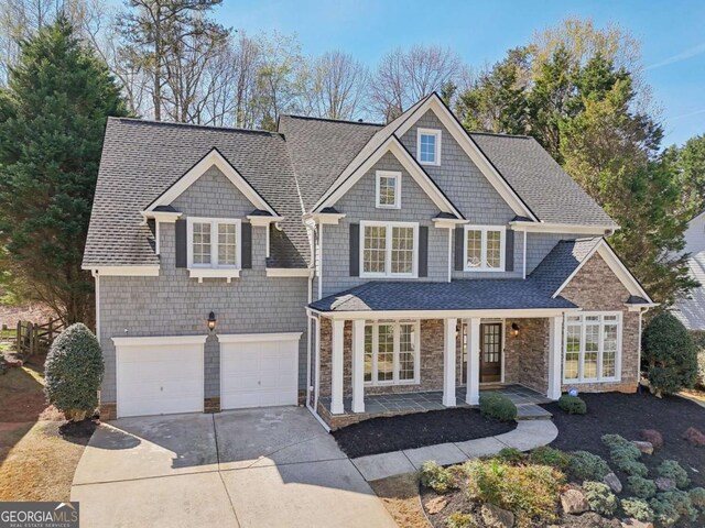 shingle-style home featuring stone siding, a porch, driveway, and a shingled roof