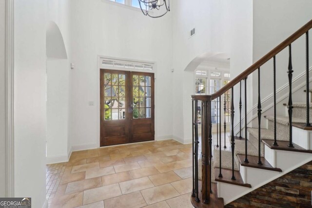 foyer entrance featuring stairs, a notable chandelier, visible vents, arched walkways, and a towering ceiling