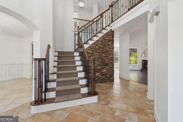 stairway featuring a lit fireplace, a high ceiling, wainscoting, a decorative wall, and arched walkways