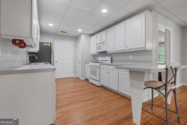1081 Katherine Ln, Greensboro, GA 30642 - kitchen with light countertops, a breakfast bar, a paneled ceiling, white appliances, and white cabinetry