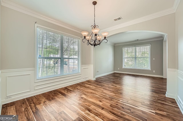 unfurnished dining area with wood finished floors, arched walkways, an inviting chandelier, a wainscoted wall, and visible vents