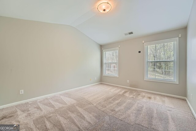 empty room featuring baseboards, vaulted ceiling, visible vents, and light colored carpet