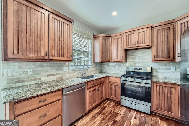 kitchen featuring stainless steel appliances, a sink, decorative backsplash, light stone counters, and dark wood-type flooring