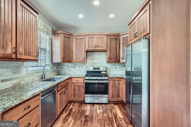 kitchen with light stone counters, a sink, decorative backsplash, appliances with stainless steel finishes, and dark wood-style flooring