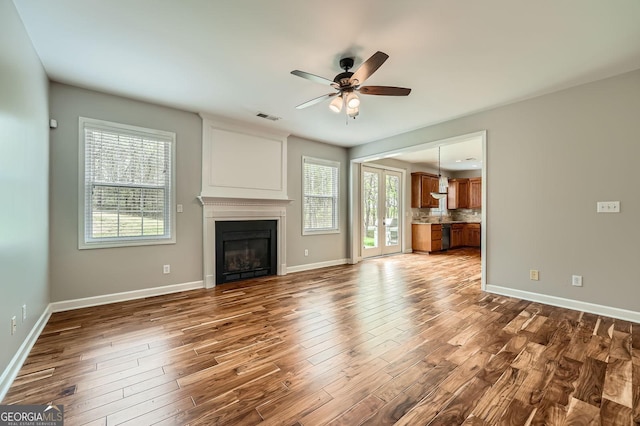 unfurnished living room featuring dark wood finished floors, visible vents, a glass covered fireplace, baseboards, and ceiling fan
