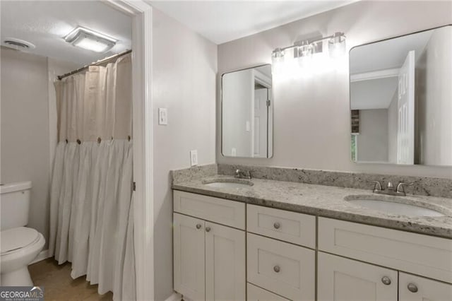full bath featuring a sink, visible vents, toilet, and double vanity