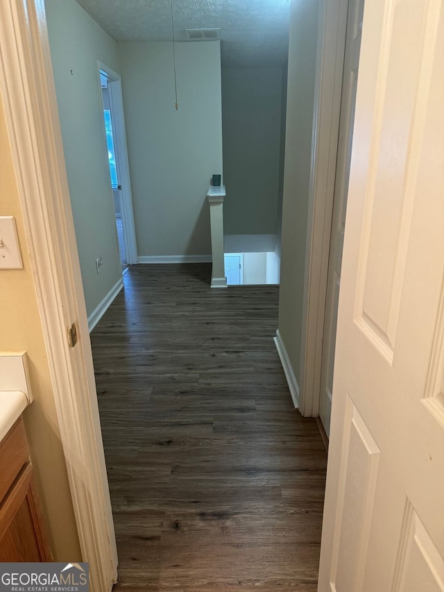 corridor featuring a textured ceiling, visible vents, dark wood-style flooring, an upstairs landing, and baseboards