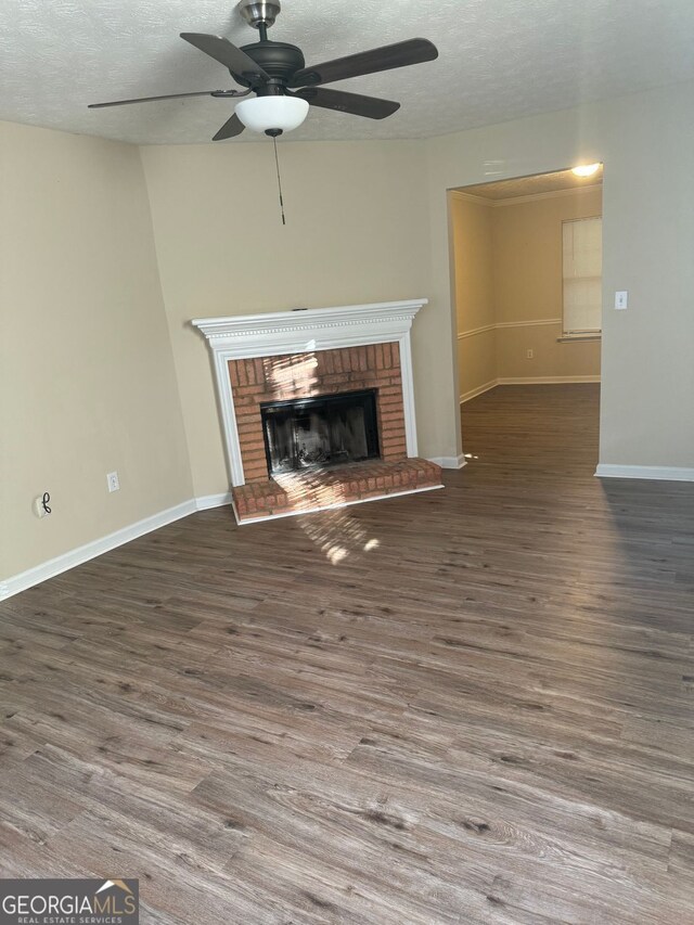 unfurnished living room with a textured ceiling, wood finished floors, a ceiling fan, and a brick fireplace