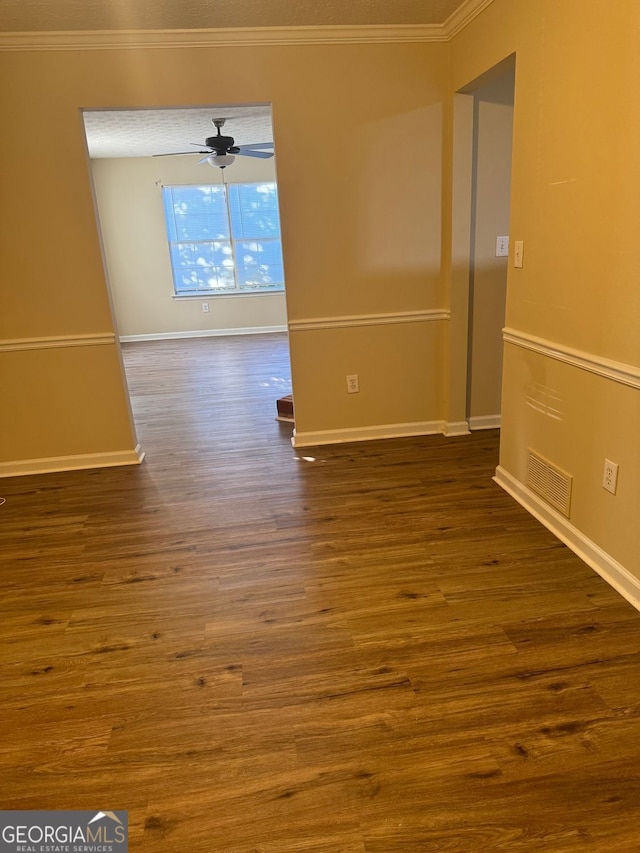 empty room with a ceiling fan, ornamental molding, visible vents, baseboards, and dark wood-style floors