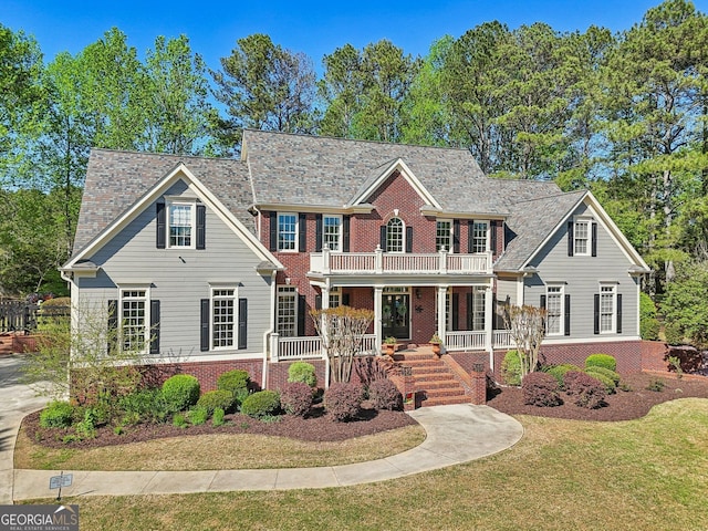 colonial home with brick siding, a front yard, covered porch, and a balcony