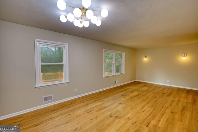spare room featuring visible vents, baseboards, light wood finished floors, and a notable chandelier