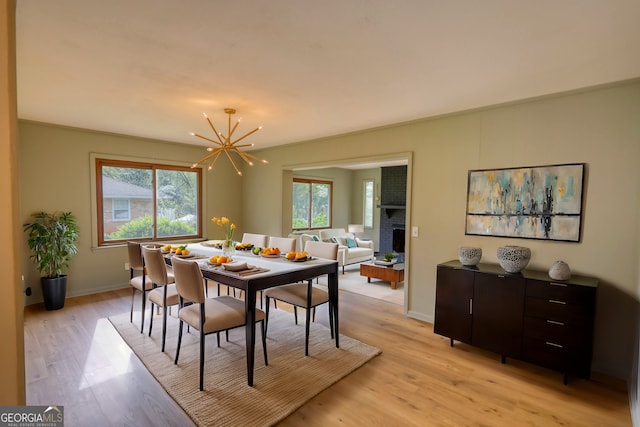 dining room featuring baseboards, light wood-type flooring, an inviting chandelier, and a brick fireplace