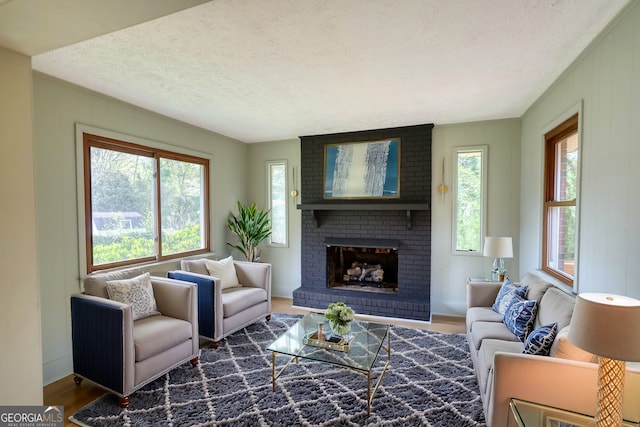 living area featuring a brick fireplace, a textured ceiling, baseboards, and wood finished floors