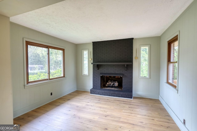 unfurnished living room featuring baseboards, a fireplace, wooden walls, a textured ceiling, and light wood finished floors