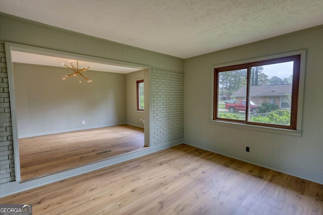 spare room with light wood-type flooring, a textured ceiling, visible vents, baseboards, and a notable chandelier
