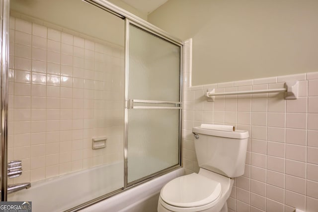 full bath featuring toilet, tile walls, enclosed tub / shower combo, and a wainscoted wall