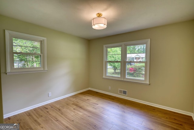 empty room with visible vents, baseboards, wood finished floors, and a healthy amount of sunlight