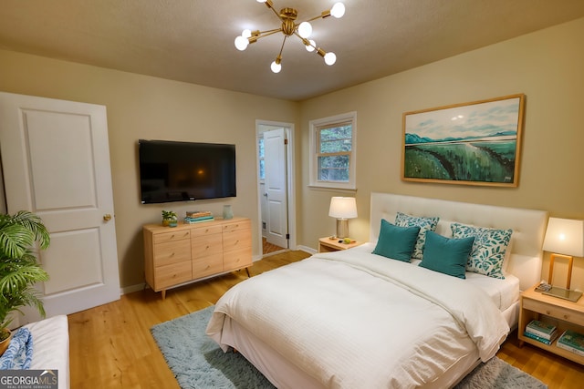 bedroom with light wood-style floors, a notable chandelier, and baseboards