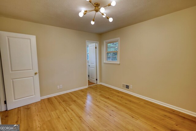 empty room with light wood-style flooring, visible vents, baseboards, and an inviting chandelier