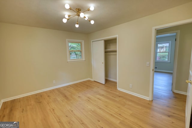 unfurnished bedroom featuring light wood-style floors, a notable chandelier, and baseboards