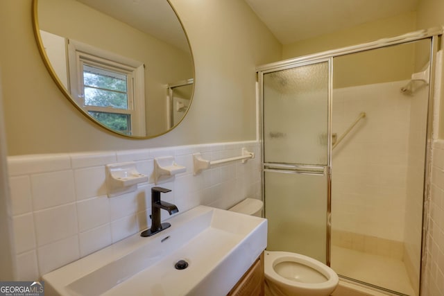 full bath featuring a shower stall, vanity, toilet, wainscoting, and tile walls