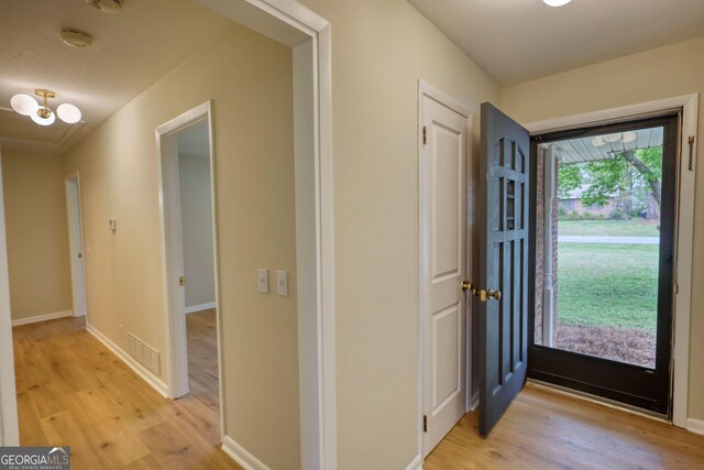 foyer entrance featuring visible vents, baseboards, light wood-type flooring, and an inviting chandelier