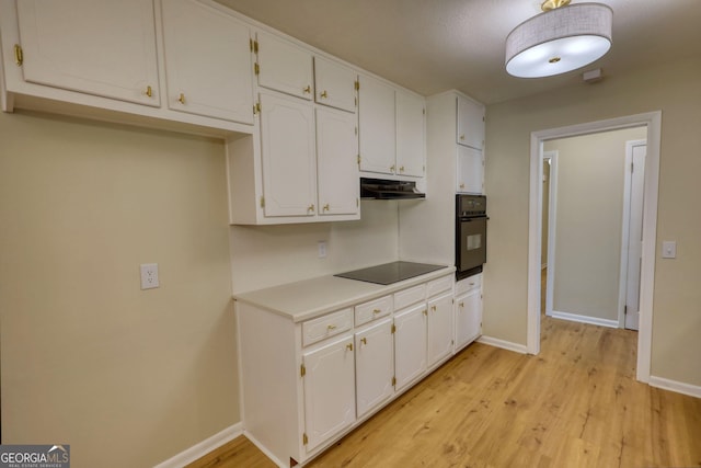 kitchen featuring under cabinet range hood, light wood finished floors, baseboards, and black appliances