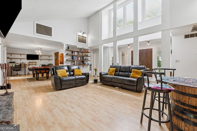 living area with visible vents, wood finished floors, a high ceiling, and an inviting chandelier