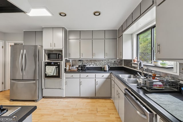 kitchen with light wood-style flooring, a sink, dark countertops, gray cabinetry, and appliances with stainless steel finishes