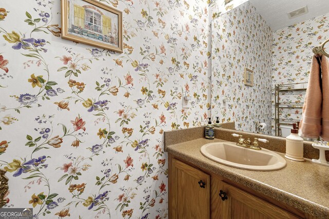 bathroom with wallpapered walls, visible vents, and vanity