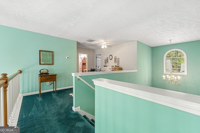 hall with an inviting chandelier, dark colored carpet, an upstairs landing, baseboards, and a textured ceiling