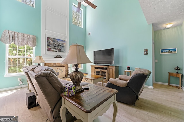 living area featuring light wood-type flooring, a textured ceiling, a ceiling fan, and baseboards