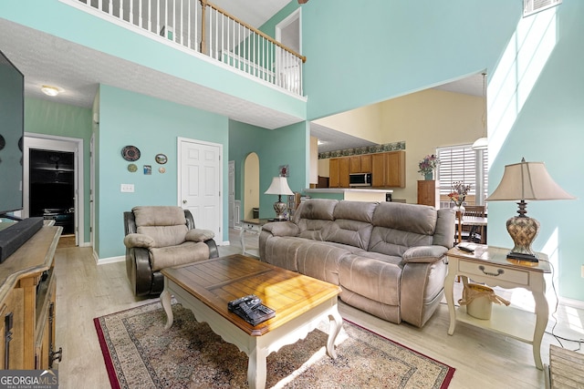 living room with baseboards, a towering ceiling, arched walkways, and light wood-style floors