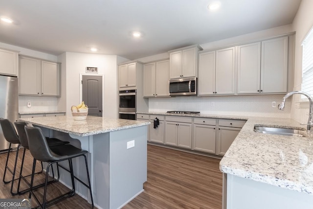 kitchen featuring a kitchen breakfast bar, a center island, dark wood-type flooring, stainless steel appliances, and a sink