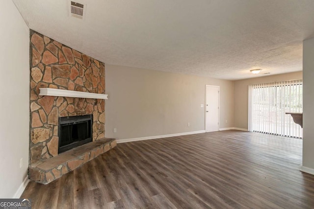 unfurnished living room with visible vents, baseboards, a stone fireplace, a textured ceiling, and wood finished floors