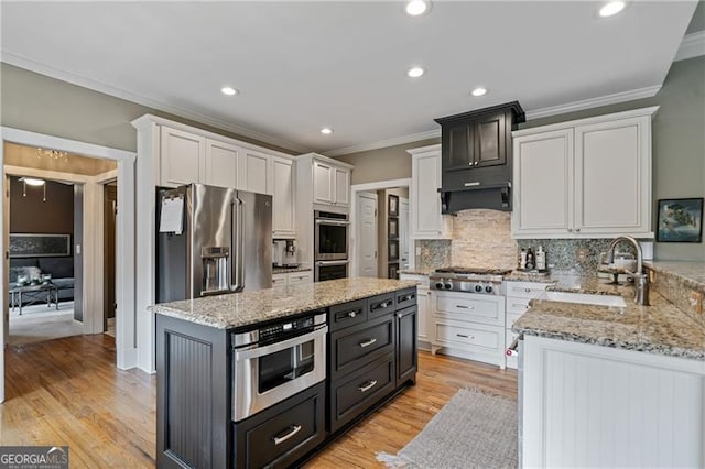 kitchen with stainless steel appliances, ornamental molding, a sink, a kitchen island, and light stone counters