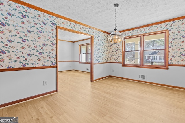 spare room with ornamental molding, visible vents, a textured ceiling, and wallpapered walls