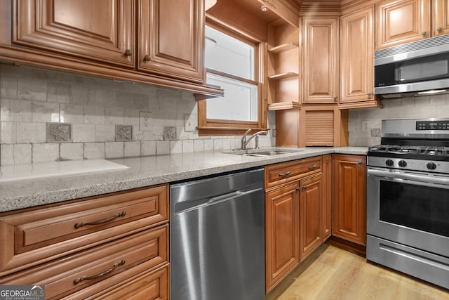 kitchen with light wood-style flooring, appliances with stainless steel finishes, light stone counters, a sink, and decorative backsplash